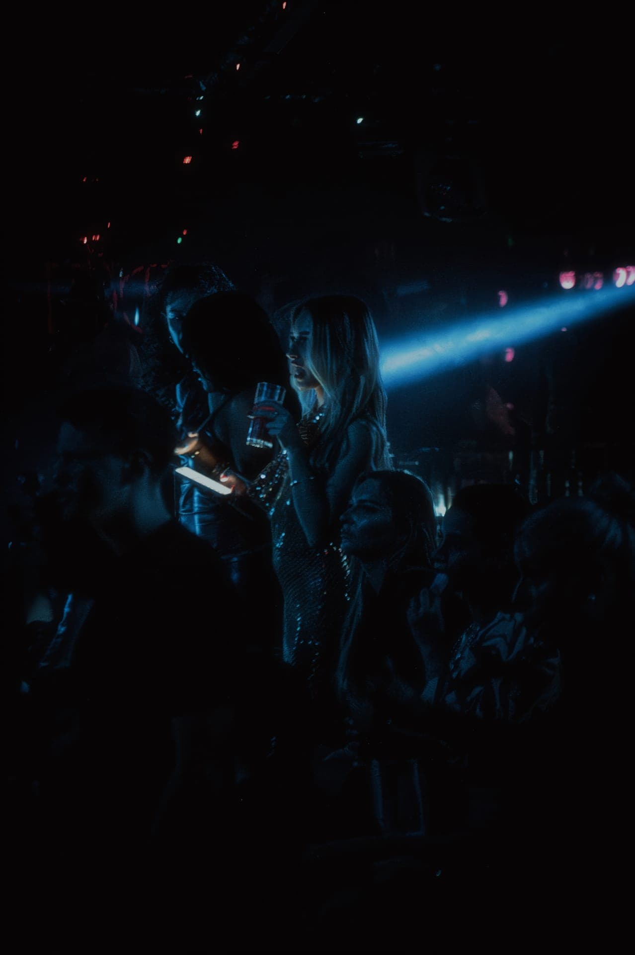 Clubbers in evening wear on a dark dance floor lit by a blue light beam