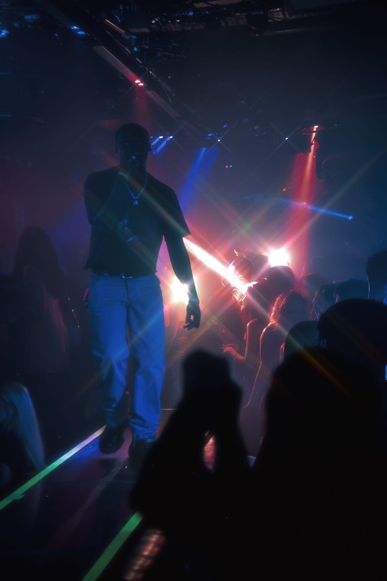 Silhouetted performer on a raised stage in a dark nightclub, with red and blue stage lights and a crowd below
