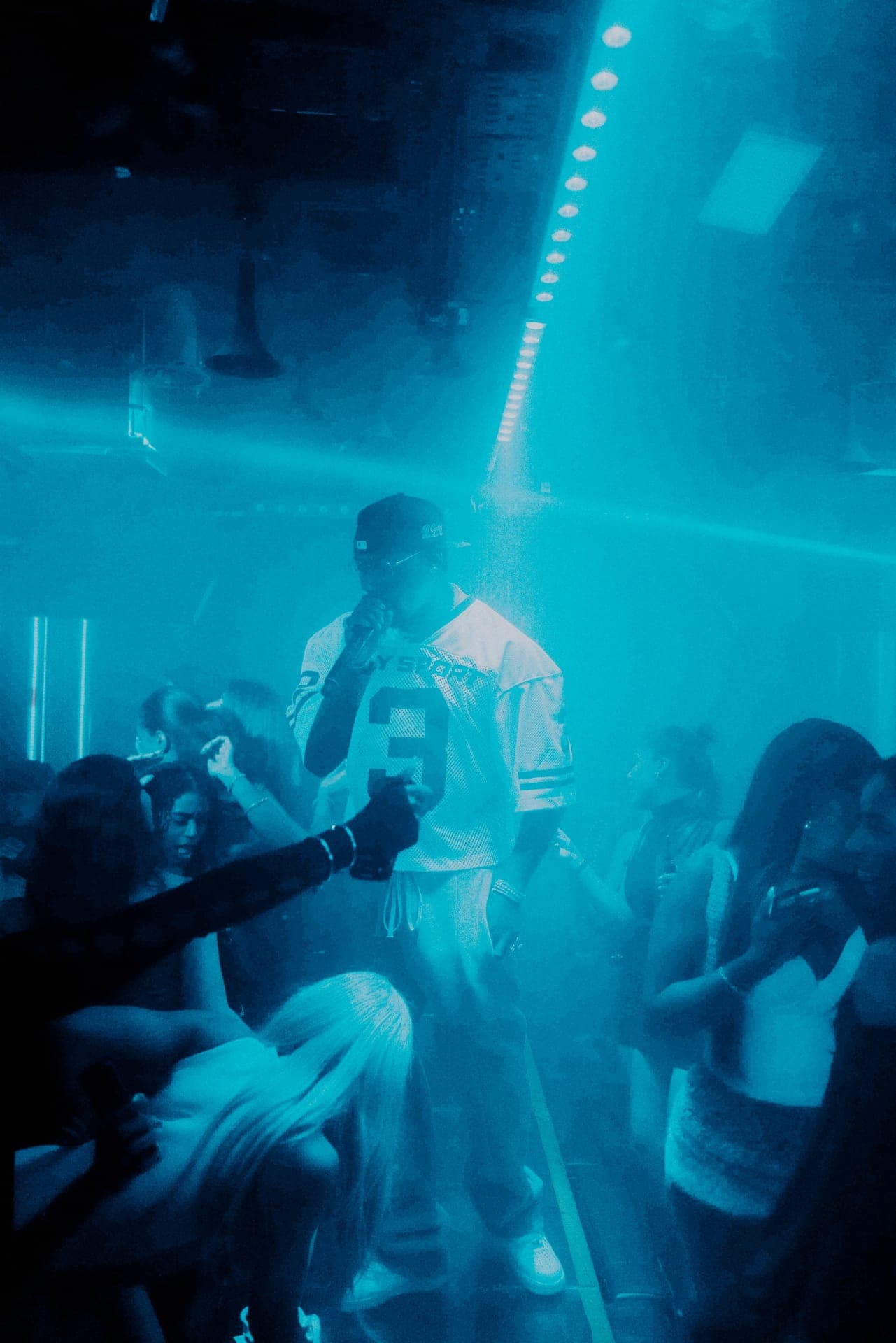 Crowd dancing in blue haze around a performer with a microphone on a club dance floor
