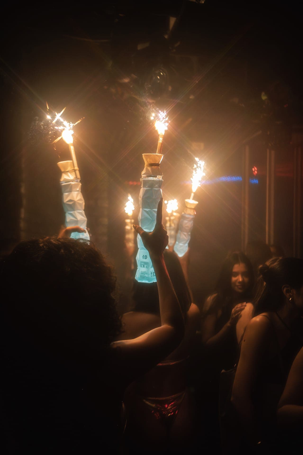 Bottles topped with lit sparklers held above a crowd in a dark nightclub